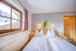 A hotel room with a bed, a window with a view of a mountain, a wooden door, and a wall-mounted lamp.