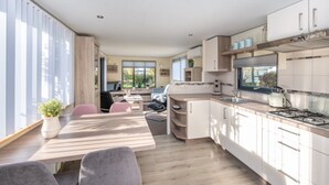 A modern kitchen with white cabinets, a gas stove, and a dining area with a wooden table and chairs. - Chalet in Goedereede Near North Sea Beach (Goedereede)