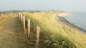 A coastal path with wooden posts, grassy dunes, and a beach with people in the distance. - Chalet in Goedereede Near North Sea Beach (Goedereede)