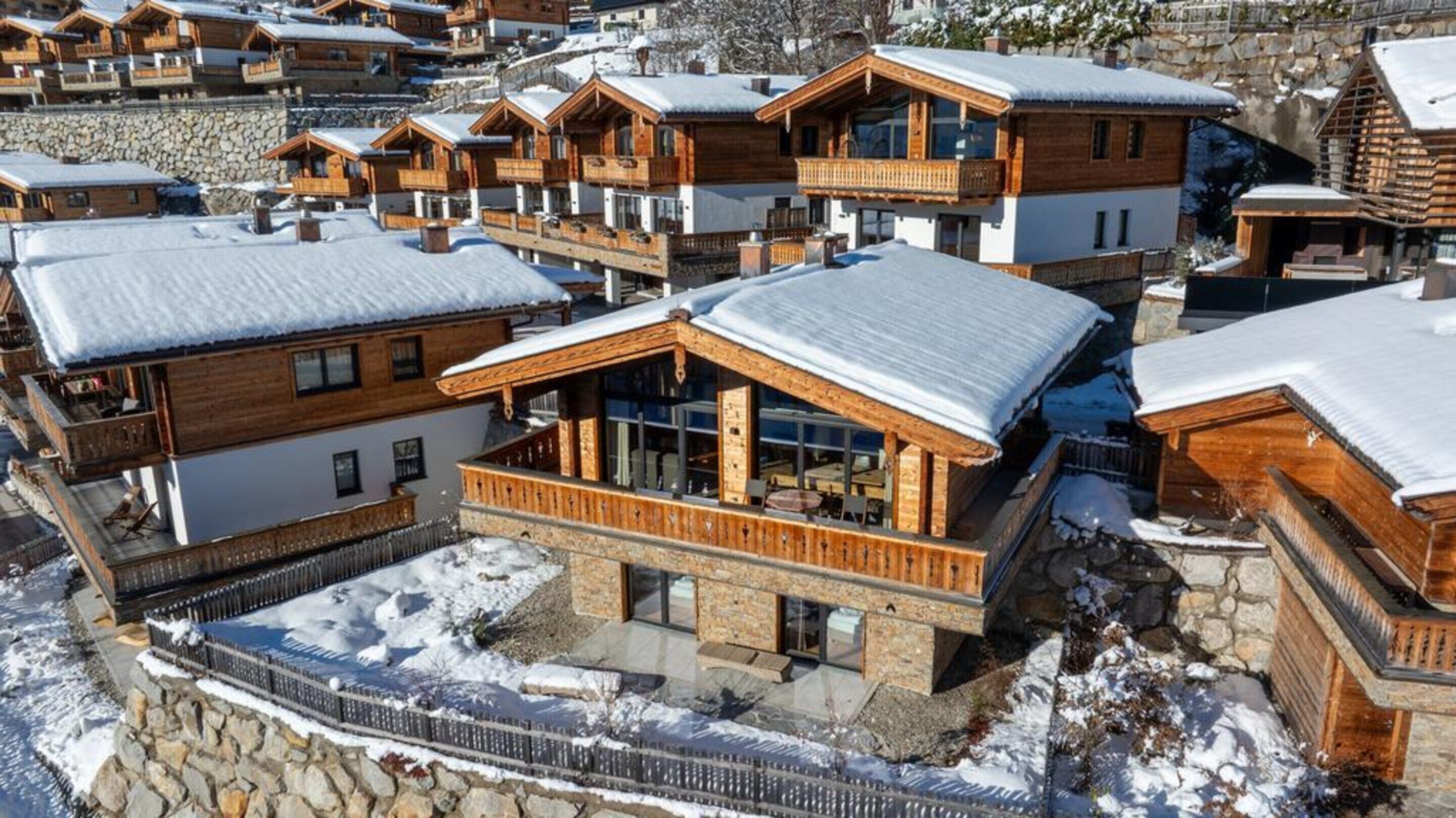 A cluster of wooden chalets with balconies, stone walls, and snow-covered roofs.