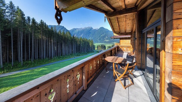 Terraza de madera con mesa y sillas, con vistas a un bosque y montañas.