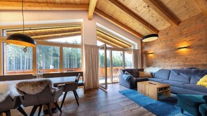 Un salón amplio con techo de madera, ventanas grandes, un sofá, una mesa baja y una mesa de comedor con sillas.