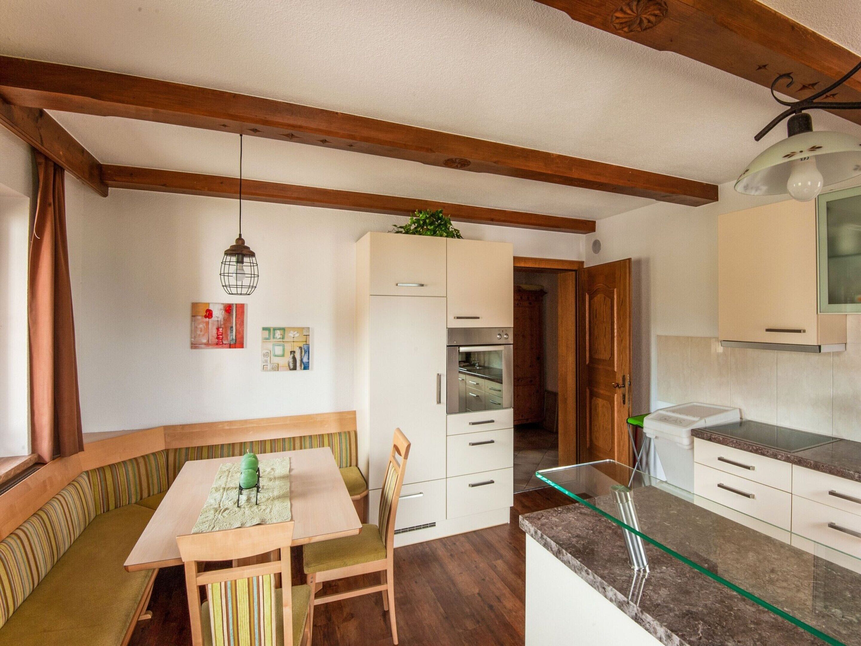 A compact kitchen with wooden beams, a dining table with chairs, and a glass countertop.