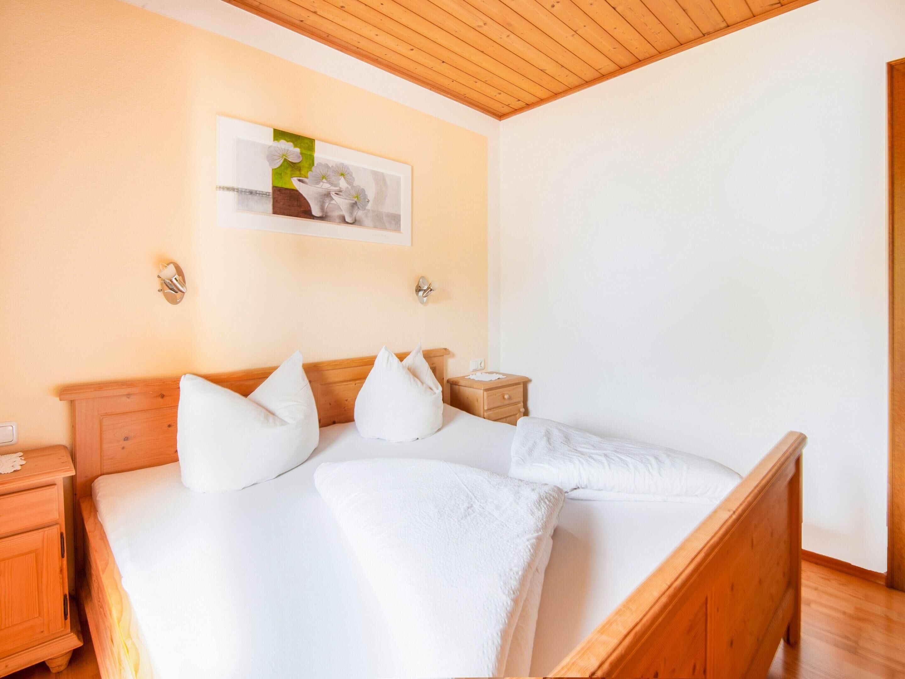 A neatly made bed with white linens and pillows, a wooden headboard, a nightstand with a lamp, and a framed picture on the wall.