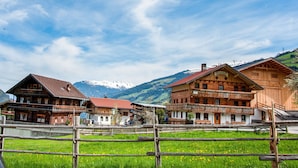 Ein traditionelles Holzchalet mit Balkon, vor einer Kulisse aus schneebedeckten Bergen und blauem Himmel.