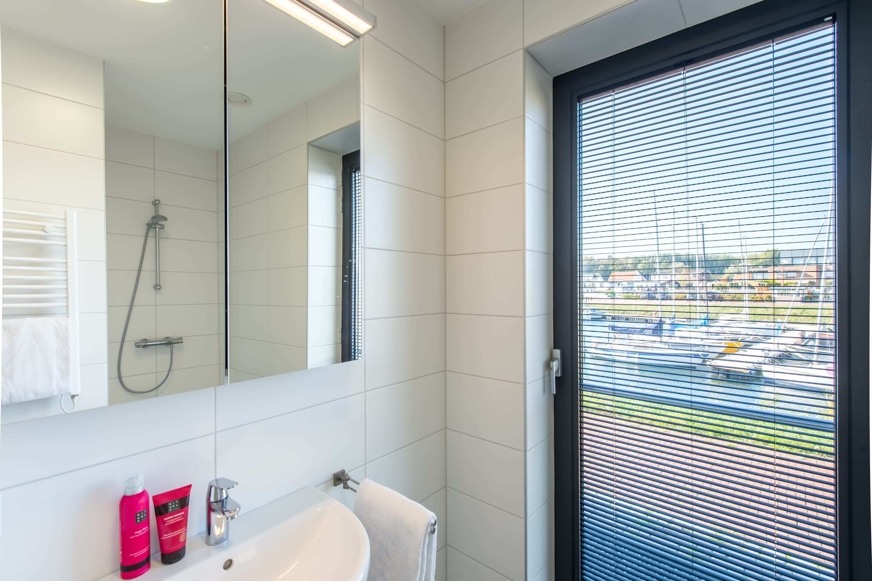 Une salle de bain moderne avec un grand miroir, une douche et une fenêtre équipée de stores.