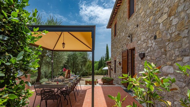 Un patio con una mesa, sillas y un paraguas amarillo, además de un edificio de piedra.