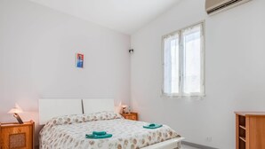 A bedroom with a bed, two bedside tables, a window, and a wooden cabinet. - Belvilla by OYO Villa Amos (Noto)
