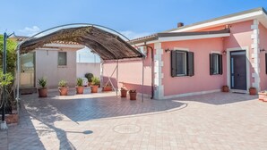A house with a covered patio area, potted plants, and a tiled courtyard. - Belvilla by OYO Villa Amos (Noto)