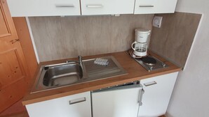Una cocina compacta con un lavamanos, dos armarios, una cafetera y un escurreplatos.