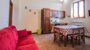 A cozy kitchen with wooden cabinets, a dining table with a colorful tablecloth, and a red sofa.