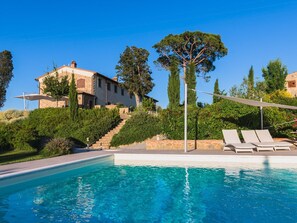 A pool with lounge chairs, a stone staircase leading to a house, and surrounding greenery.