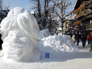 Una escultura de nieve con forma de rostro, una calle nevada y edificios con letreros.