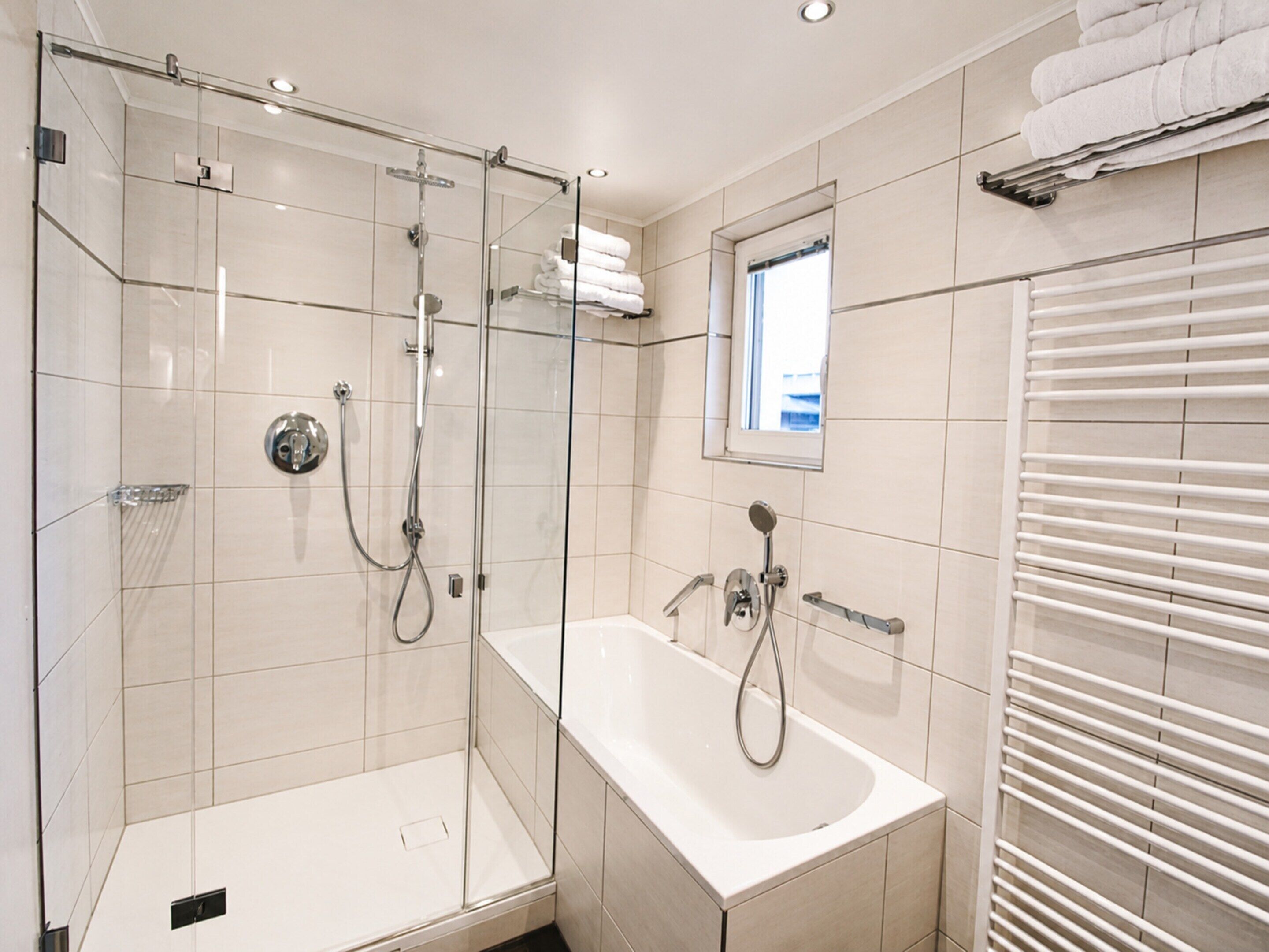 A modern bathroom with a glass-enclosed shower, a standalone bathtub, and a window providing natural light.