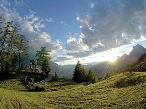 Un paisaje montañoso con cielo despejado, un puente de madera y un pico de montaña lejano.