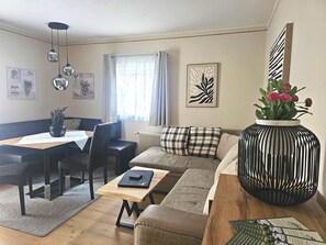 Un salon moderne comprenant un coin repas, un ensemble de canapés, une table basse, un vase avec des fleurs et un radiateur.