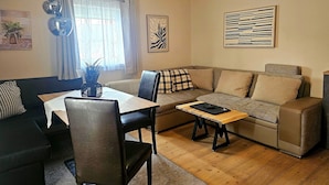 A living room with a sofa, a dining table with chairs, a coffee table, and artwork on the walls. - Apartment in Seefeld Near Rosshutte Ski Resort (Seefeld in Tirol)
