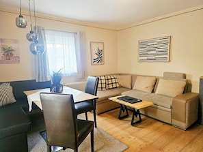 A living room with a sofa, a dining table with chairs, a coffee table, and artwork on the walls.