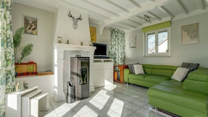 A modern living room with a green sofa, a fireplace, and a kitchen area. - Holiday Home in Heuvelland With Garden (Heuvelland)