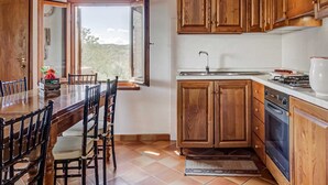 A kitchen with wooden cabinets, a dining table with chairs, a window, and a view of the outdoors. - Rustic Tuscan Stonehouse (Gambassi Terme)