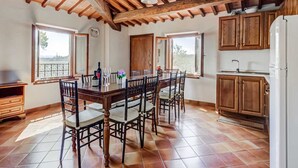 A spacious dining area with a wooden table and chairs, large windows, and a kitchen with wooden cabinets. - Rustic Tuscan Stonehouse (Gambassi Terme)