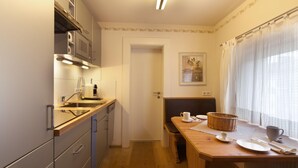 Une cuisine compacte équipée d’un four à micro-ondes, d’un évier et de placards. On y trouve également un coin repas avec une table, des chaises et un panier. Une porte donne accès à une autre pièce.