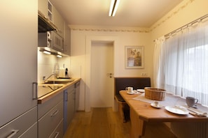 A compact kitchen with a microwave, sink, and cabinets. There's a dining area with a table, chairs, and a basket. A door leads to another room.