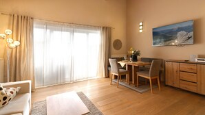 Une pièce avec un plafond en bois, une table à manger avec des chaises, un canapé, un téléviseur fixé au mur et une fenêtre avec des rideaux.