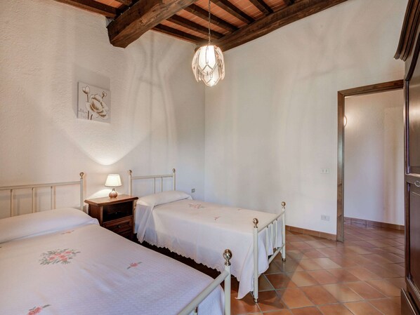 A bedroom with two single beds, a nightstand with a lamp, a wooden ceiling, and a door to the right.