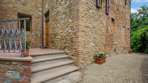 A stone building with a wooden door, steps leading to a gravel driveway, and a metal railing. - Varna Charm: Tuscan Getaway (Gambassi Terme)