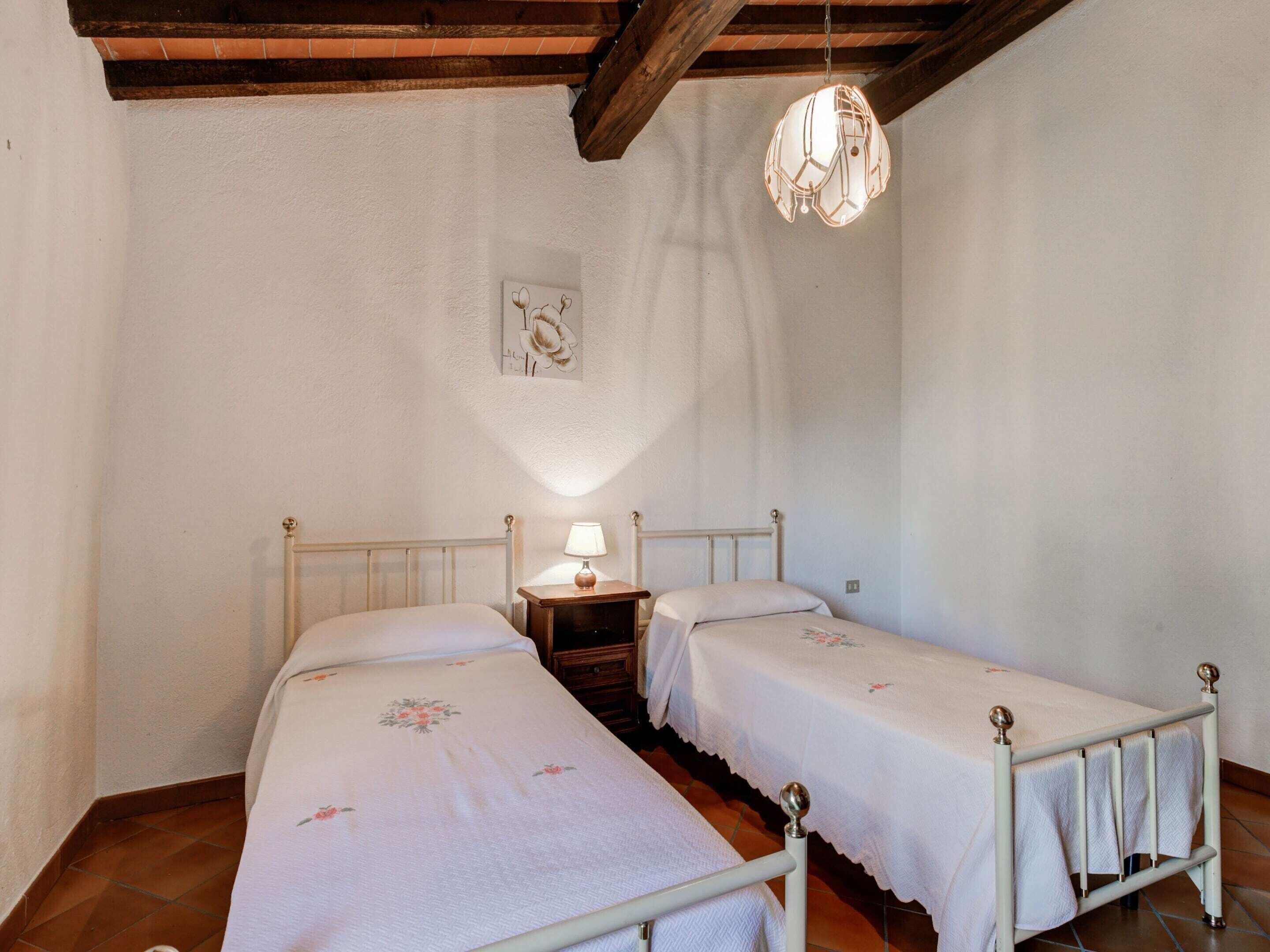 A bedroom with two beds, a nightstand with a lamp, a wall-mounted artwork, and a hanging light fixture.