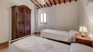 A bedroom with two beds, a wooden wardrobe, a radiator, and a window. - Varna Charm: Tuscan Getaway (Gambassi Terme)