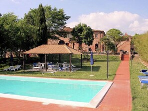 A swimming pool with lounge chairs and a gazebo, surrounded by greenery and a brick building in the background. - Agriturismo in Tuscany With Pool and Wine Tasting (Peccioli)