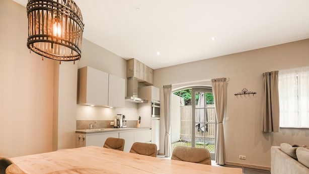A modern kitchen with a dining area, a large wooden table, and a view of a garden through an open door. - Scenic Escape With Garden (Grubbenvorst)