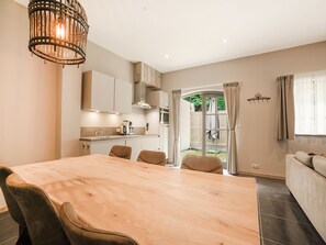 Une cuisine moderne avec un coin repas, une grande table en bois et une vue sur un jardin, accessible par une porte ouverte.