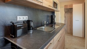 A modern kitchen with a black countertop, a coffee maker, a toaster, and a microwave. There are wooden cabinets and a white door in the background. - Ideal Holiday Home in Wutha-Farnroda near City Center (Wutha-Farnroda)
