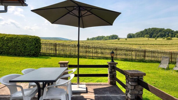 An outdoor patio with a table and chairs, a large umbrella, and a view of a fenced field and hills in the background. - Ideal Holiday Home in Wutha-Farnroda near City Center (Wutha-Farnroda)