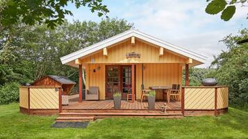 A wooden cabin with a deck, a dining area with chairs and a table, and a sign that reads 'Hohen'.