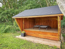 Una estructura de madera con techo inclinado, una plataforma y dos sillas.