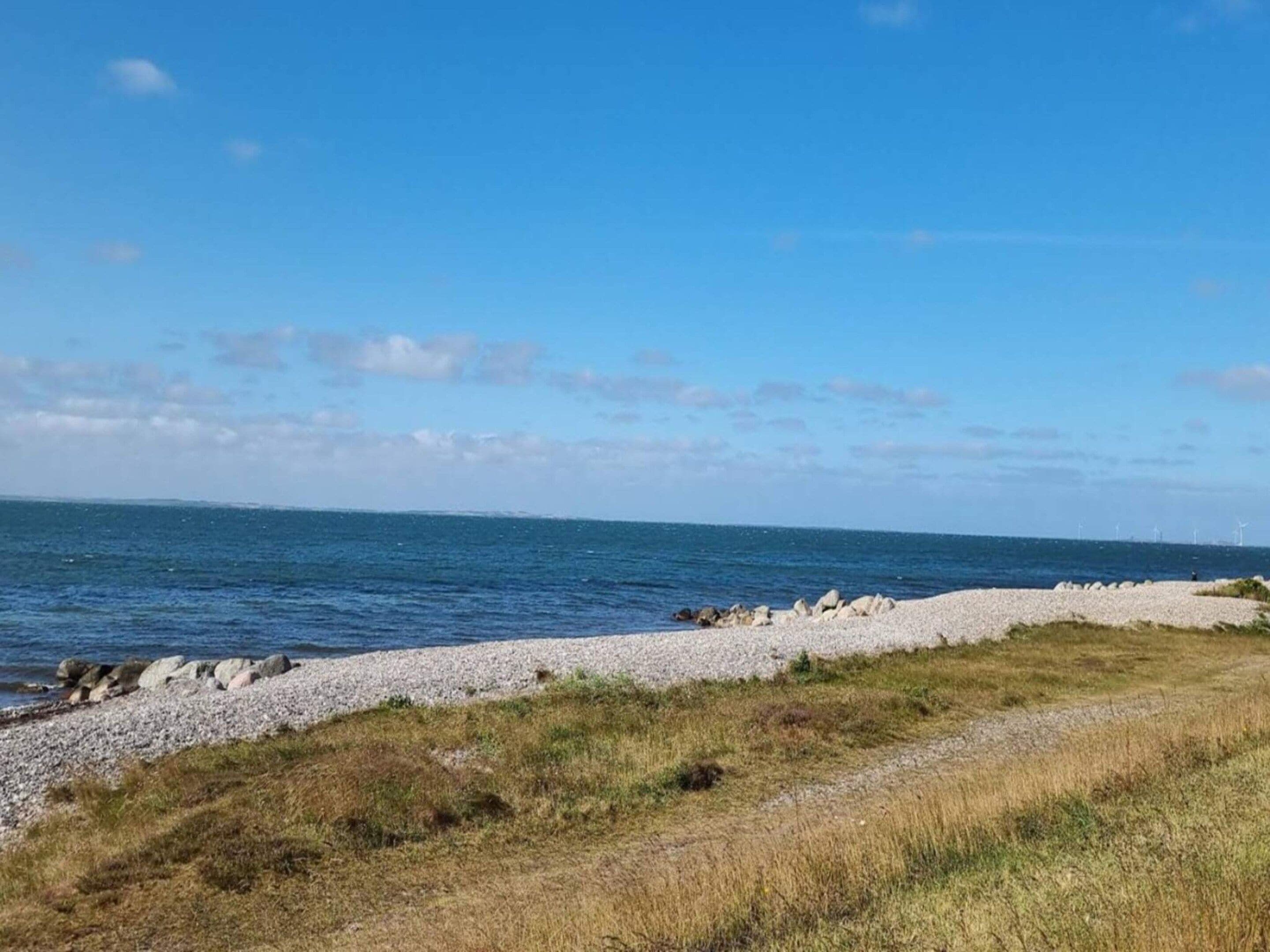 A coastal landscape with a pebble beach, grassy areas, and a clear blue sky.