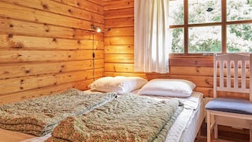 A wooden cabin room with a bed, two pillows, a chair, and a window with curtains.