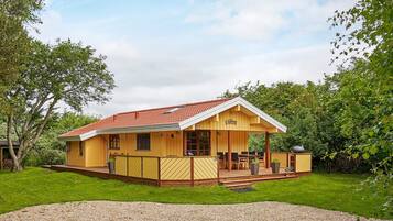 A yellow wooden house with a red roof, a covered porch, and a gravel driveway.