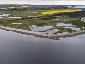 Eine Luftaufnahme einer Küstenlandschaft mit Sandstrand, grünen Feldern und gelben Getreidefeldern.