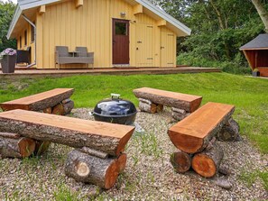 En stuga av trä med en veranda, utomhusmöbler och en grill.