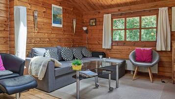 A cozy cabin interior with a sofa, armchair, and a small table with a plant.