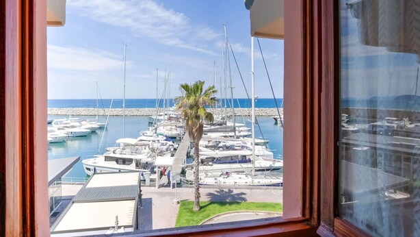 A marina with multiple boats docked, a palm tree, and a clear blue sky. - Belvilla by Oyo Grecale 3 (San Vincenzo)