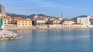 A coastal town with buildings along the waterfront, a clear sky, and a rocky outcrop with a sign. - Belvilla by Oyo Grecale 3 (San Vincenzo)