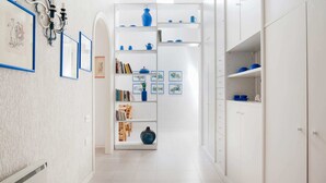 A hallway with white walls, a white tiled floor, and a white shelving unit with blue accents. - Belvilla by Oyo Grecale 3 (San Vincenzo)