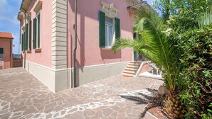 A pink building with green shutters, a stone-paved entrance, and a staircase leading to a balcony. - Belvilla by Oyo Grecale 3 (San Vincenzo)