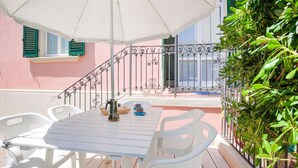 A white table with chairs under a white umbrella, a metal railing, and a pink building in the background. - Belvilla by Oyo Grecale 3 (San Vincenzo)